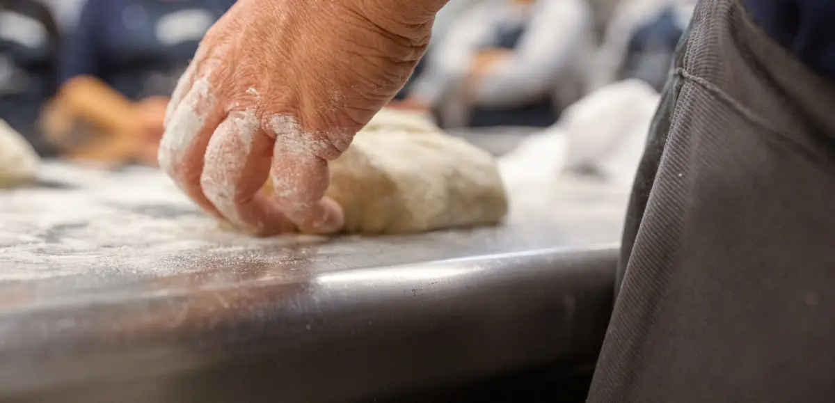Bemehlte Hand am Teig, Nahaufnahme auf Höhe der Arbeitsfläche