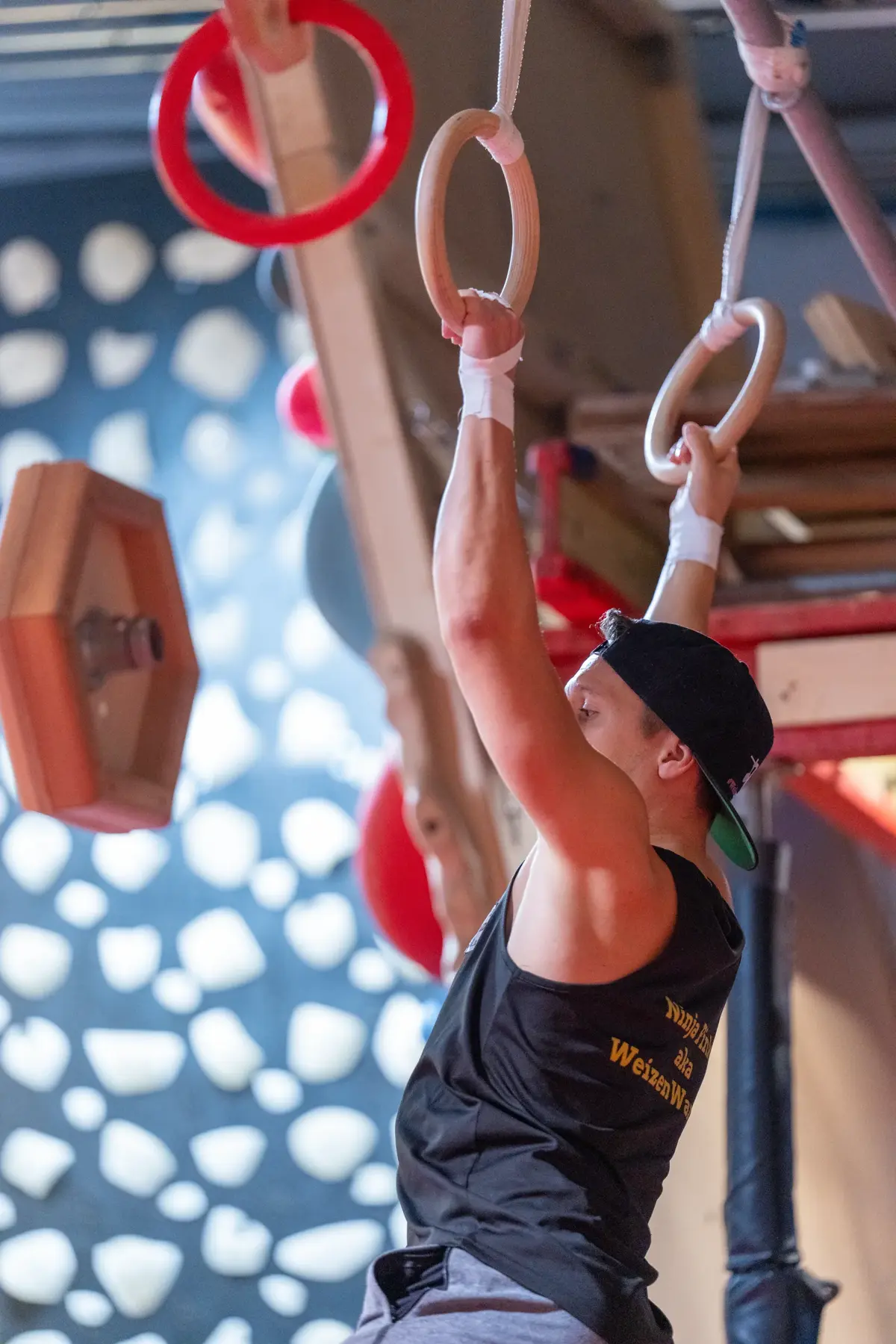 Athlet hängt an Turnringen vor einer Kletterwand